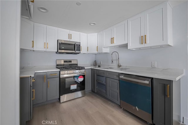 kitchen with appliances with stainless steel finishes, gray cabinetry, light wood-type flooring, white cabinetry, and a sink