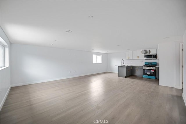 unfurnished living room featuring light wood-style flooring, baseboards, and a sink