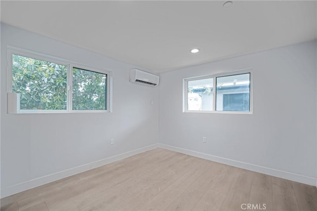 unfurnished room featuring recessed lighting, a wall unit AC, light wood-style flooring, and baseboards