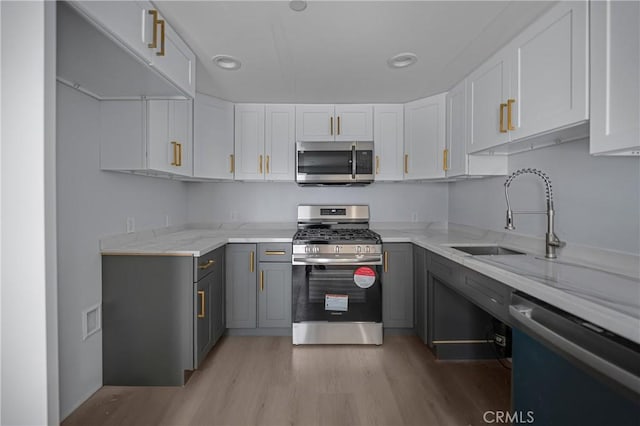 kitchen featuring light stone counters, stainless steel appliances, a sink, and gray cabinetry