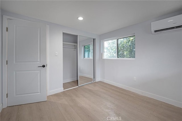 unfurnished bedroom with baseboards, an AC wall unit, light wood-type flooring, a closet, and recessed lighting