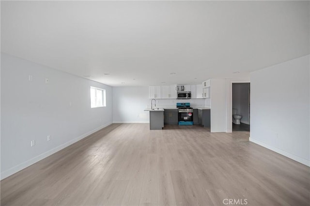 unfurnished living room with light wood finished floors, a sink, and baseboards