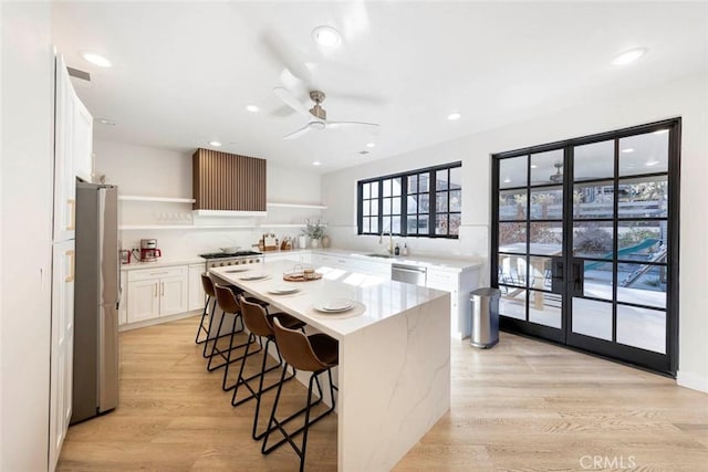 kitchen featuring appliances with stainless steel finishes, a breakfast bar, light wood-style floors, open shelves, and a sink