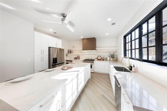 kitchen featuring open shelves, appliances with stainless steel finishes, light wood-style floors, a sink, and light stone countertops