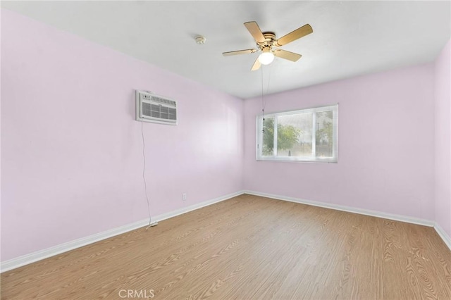 spare room featuring ceiling fan, an AC wall unit, light wood-type flooring, and baseboards