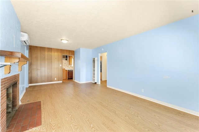 unfurnished living room with a textured ceiling, baseboards, light wood-type flooring, a brick fireplace, and a wall mounted air conditioner