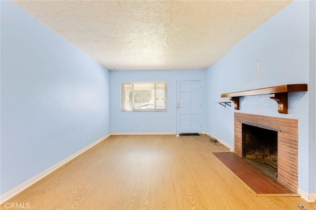 unfurnished living room with a brick fireplace, a textured ceiling, and wood finished floors