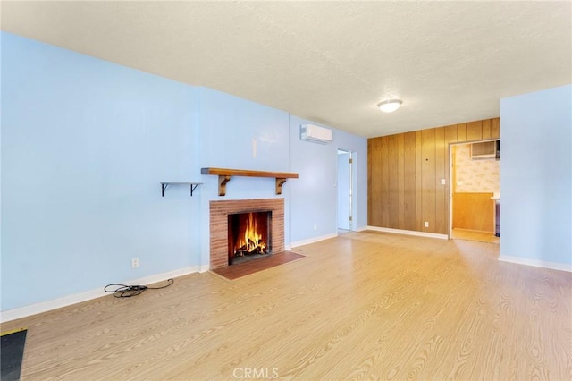 unfurnished living room featuring baseboards, wood finished floors, a textured ceiling, a fireplace, and a wall mounted AC