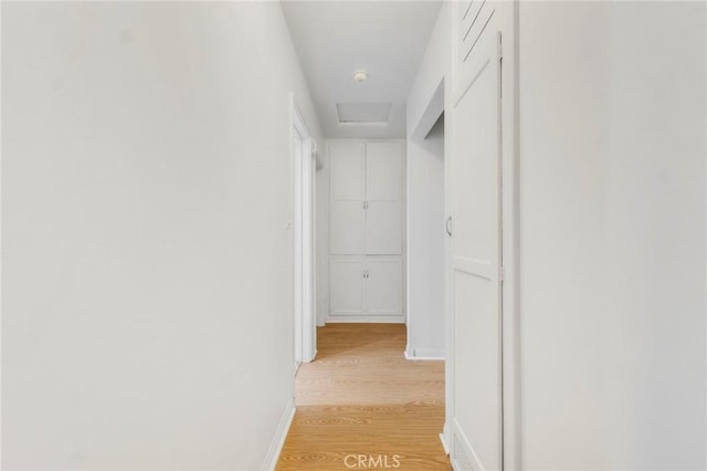 hallway with attic access, light wood-style flooring, and baseboards