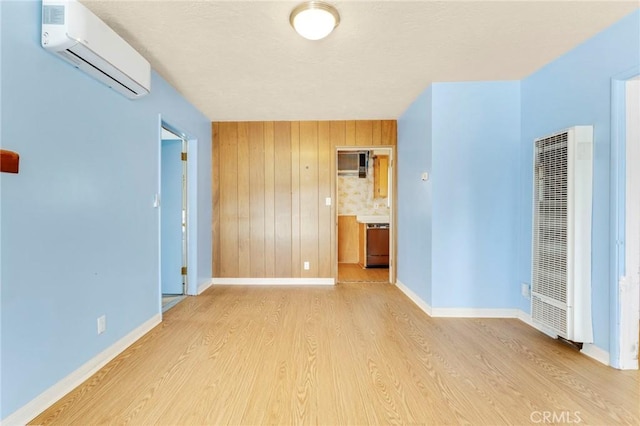 empty room with light wood-type flooring, a heating unit, a wall mounted air conditioner, and baseboards