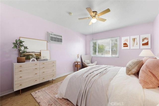 bedroom featuring light wood-type flooring, a wall mounted air conditioner, a ceiling fan, and baseboards