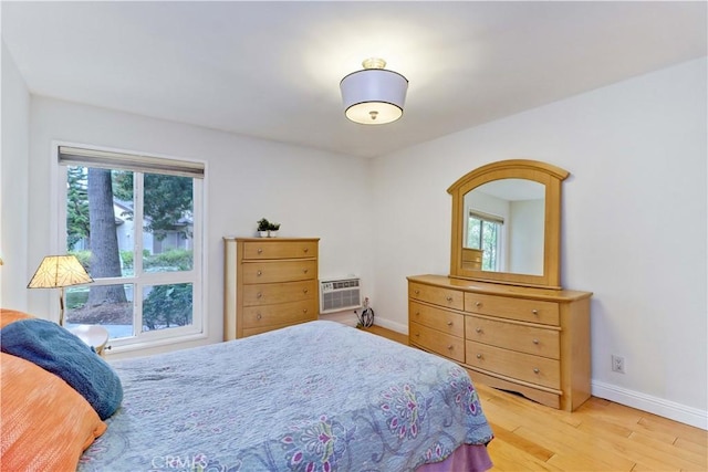 bedroom featuring light wood-type flooring, multiple windows, a wall unit AC, and baseboards