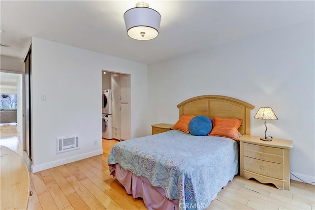 bedroom featuring light wood-type flooring, baseboards, visible vents, and stacked washing maching and dryer