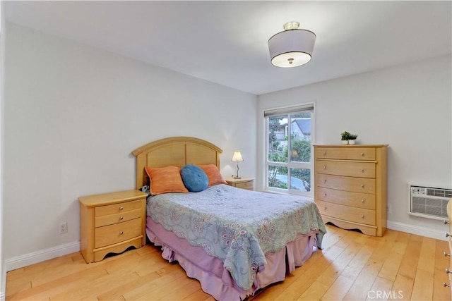 bedroom with an AC wall unit, light wood-style flooring, and baseboards