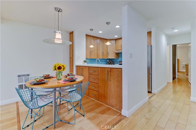 kitchen featuring light wood-style floors, freestanding refrigerator, decorative backsplash, and brown cabinetry