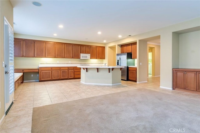 kitchen featuring white microwave, light colored carpet, built in study area, brown cabinetry, and stainless steel fridge