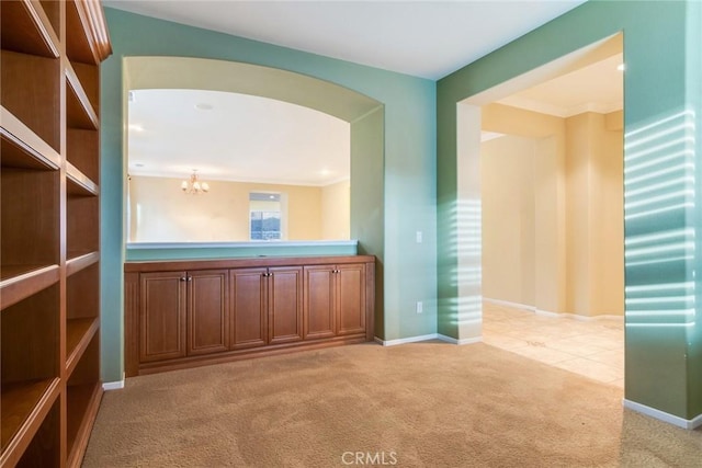 spare room with light carpet, baseboards, arched walkways, and a chandelier