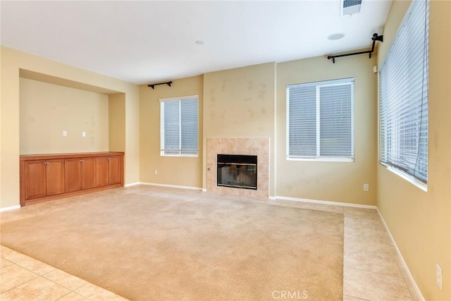 unfurnished living room with light tile patterned floors, light colored carpet, a high end fireplace, baseboards, and visible vents