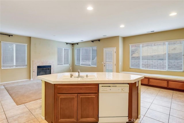 kitchen with tile countertops, white dishwasher, a sink, open floor plan, and a glass covered fireplace