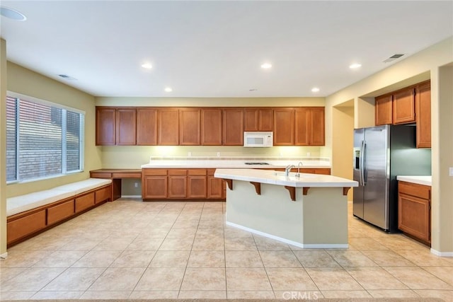 kitchen with stainless steel refrigerator with ice dispenser, light countertops, white microwave, brown cabinetry, and built in study area