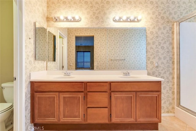 full bathroom featuring toilet, wallpapered walls, double vanity, and a sink