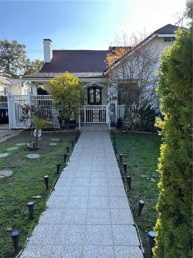 view of front of home with a shingled roof, a chimney, a front yard, and fence