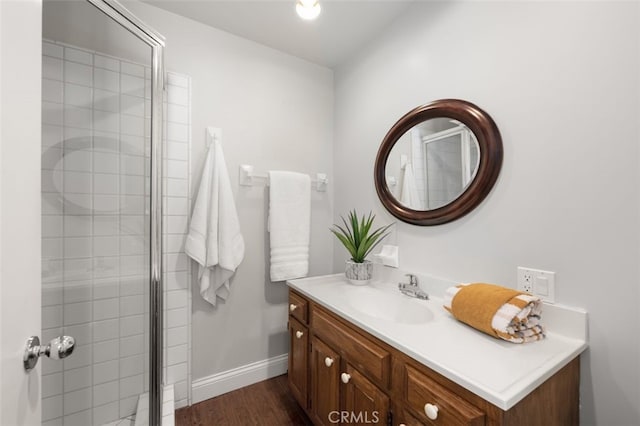 bathroom featuring a tile shower, vanity, baseboards, and wood finished floors