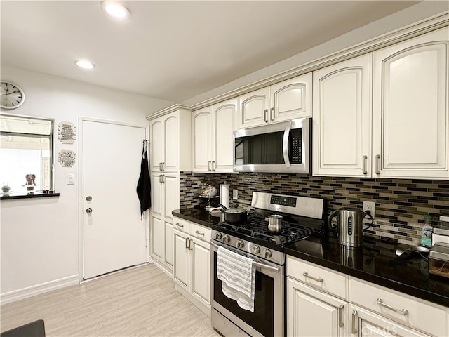 kitchen featuring appliances with stainless steel finishes, dark countertops, light wood-style flooring, and tasteful backsplash