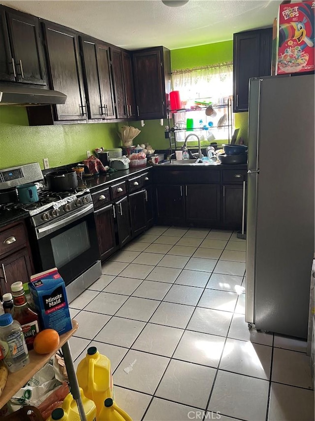 kitchen featuring light tile patterned floors, under cabinet range hood, a sink, appliances with stainless steel finishes, and dark countertops