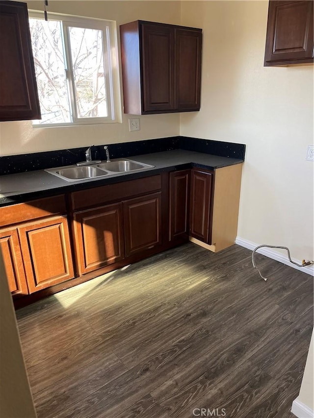 kitchen with dark wood-type flooring, dark countertops, a sink, and baseboards