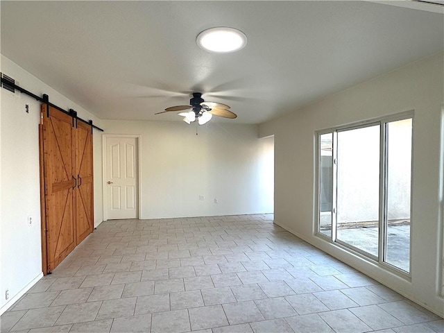 empty room with a barn door, baseboards, and a ceiling fan