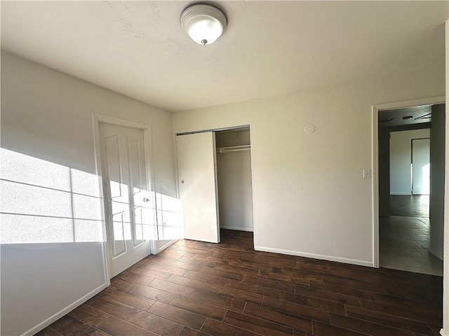 unfurnished bedroom with dark wood-type flooring, a closet, and baseboards