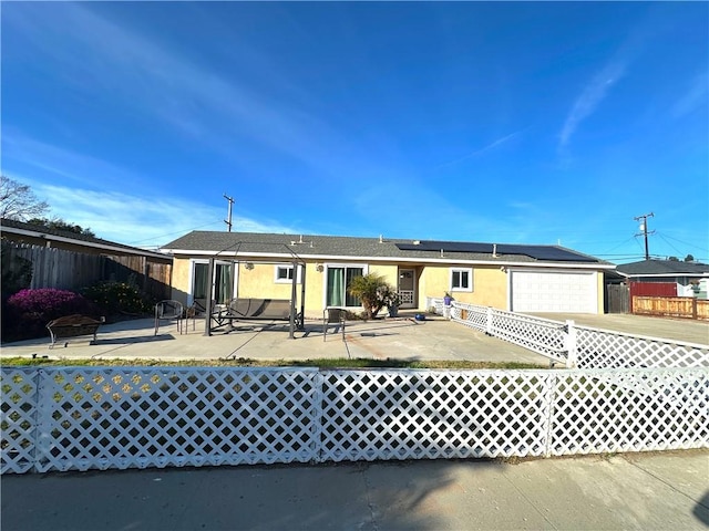 view of front facade featuring fence, driveway, stucco siding, a patio area, and roof mounted solar panels