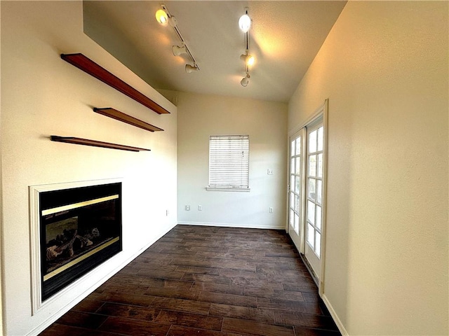 unfurnished living room with vaulted ceiling, dark wood-style flooring, a glass covered fireplace, and baseboards