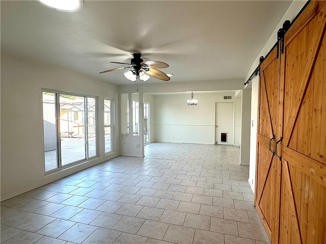 unfurnished room featuring a barn door, baseboards, ceiling fan with notable chandelier, a textured ceiling, and light tile patterned flooring