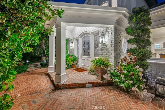 view of exterior entry featuring covered porch and brick siding