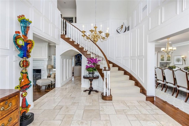 staircase with stone tile floors, a towering ceiling, ornamental molding, a fireplace, and a chandelier