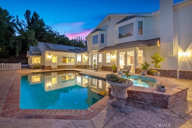 pool at dusk with a patio area, an outdoor pool, and an in ground hot tub