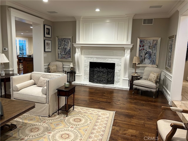 living area with crown molding, visible vents, a decorative wall, a high end fireplace, and wood finished floors