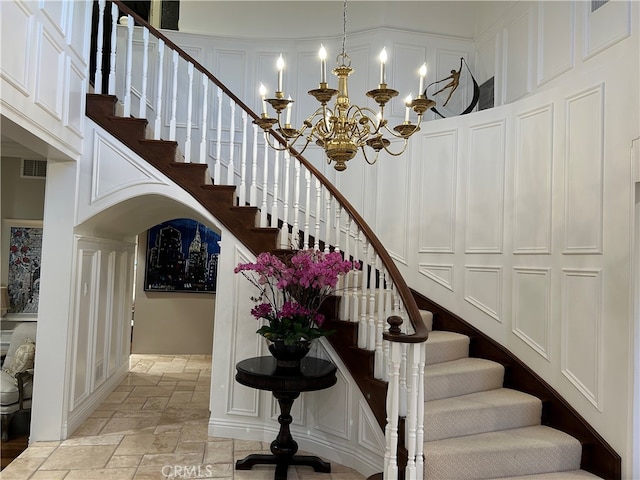 stairs featuring arched walkways, a notable chandelier, a decorative wall, stone tile floors, and visible vents