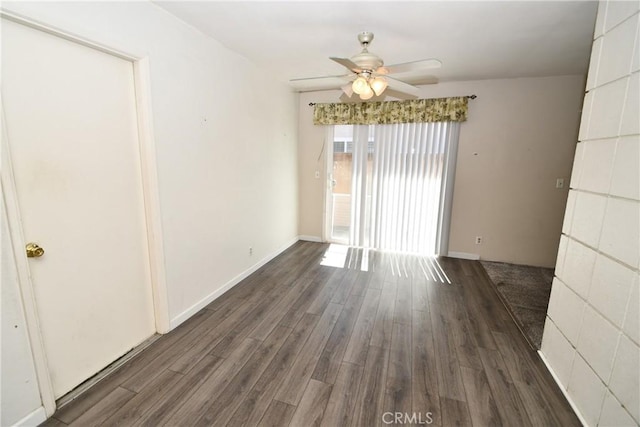 spare room featuring dark wood-type flooring, a ceiling fan, and baseboards