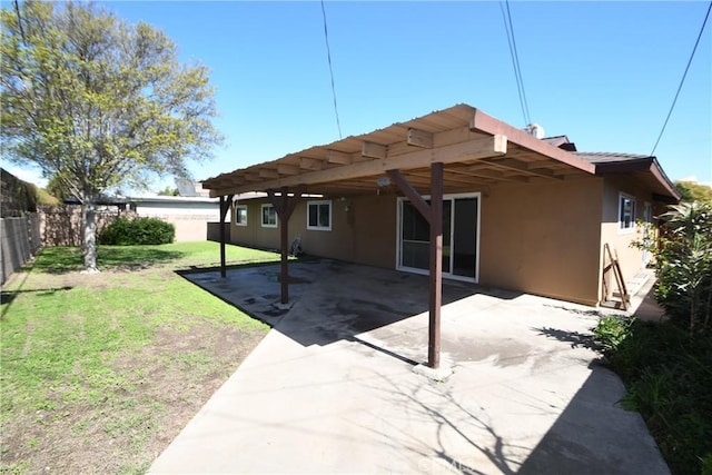 rear view of property featuring a patio, fence, a lawn, and stucco siding