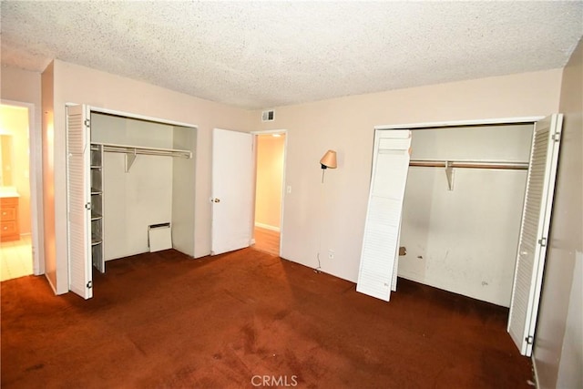 unfurnished bedroom featuring a textured ceiling, carpet flooring, two closets, and visible vents