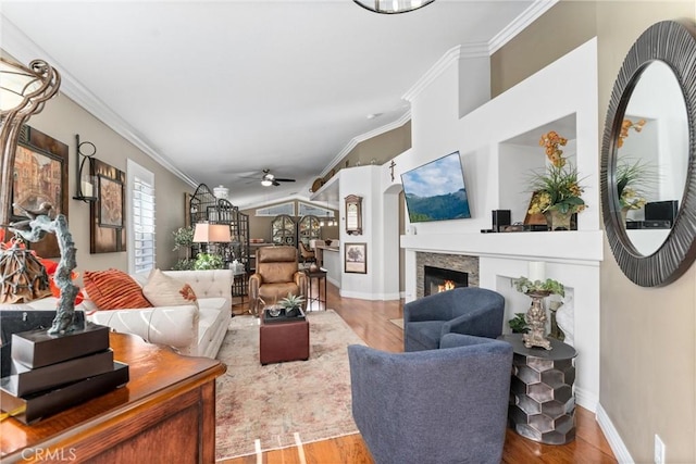 living area with ornamental molding, a lit fireplace, and wood finished floors