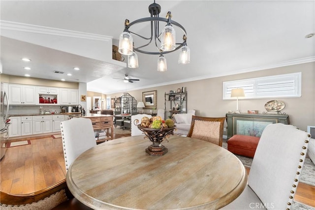 dining area with light wood finished floors, recessed lighting, crown molding, and ceiling fan with notable chandelier