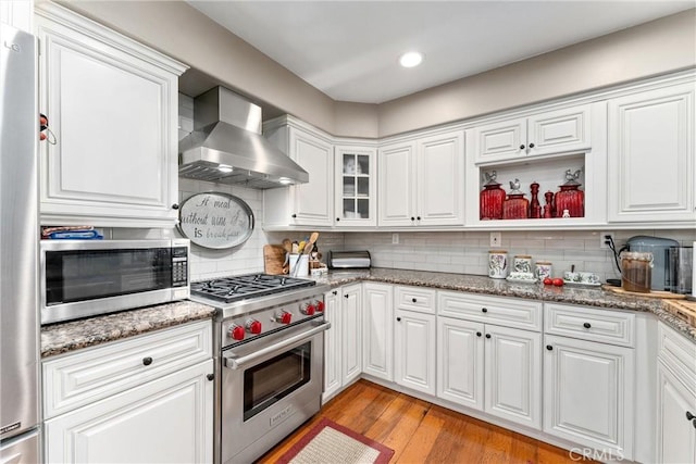 kitchen featuring light wood-style flooring, stainless steel appliances, white cabinets, wall chimney exhaust hood, and tasteful backsplash