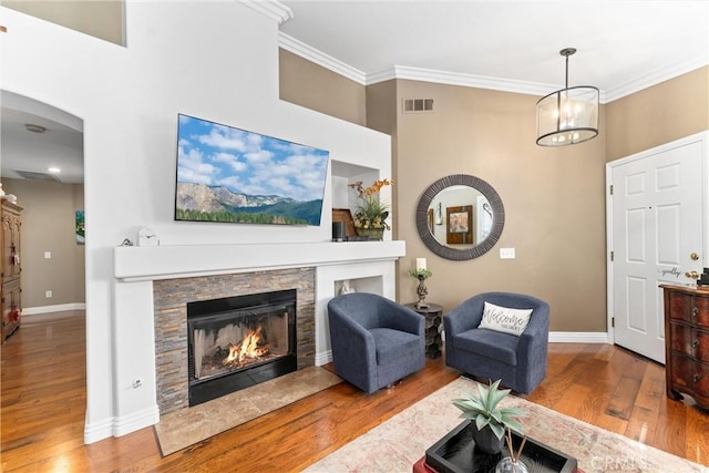 living area featuring ornamental molding, visible vents, a stone fireplace, and wood finished floors