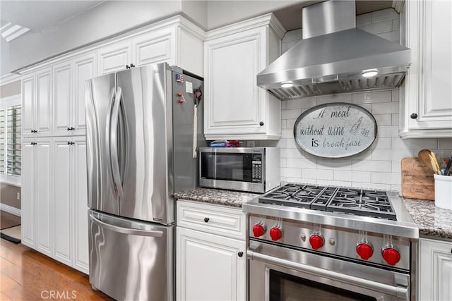 kitchen featuring stainless steel appliances, wall chimney range hood, backsplash, and white cabinets