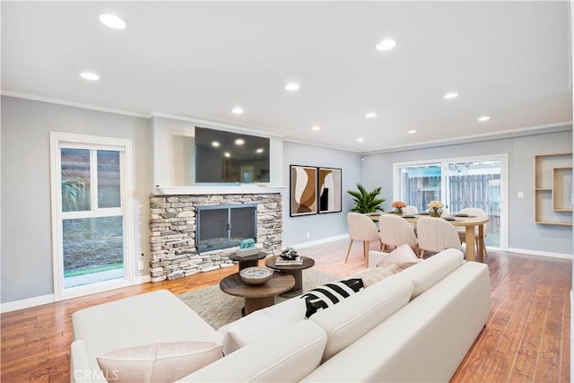 living room featuring recessed lighting, ornamental molding, a stone fireplace, wood finished floors, and baseboards