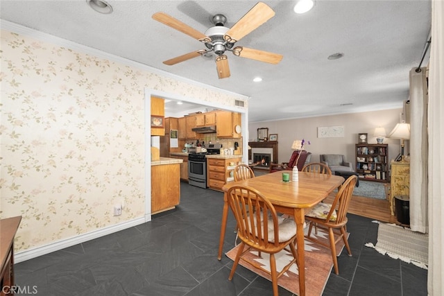 dining area featuring ornamental molding, a lit fireplace, baseboards, and wallpapered walls